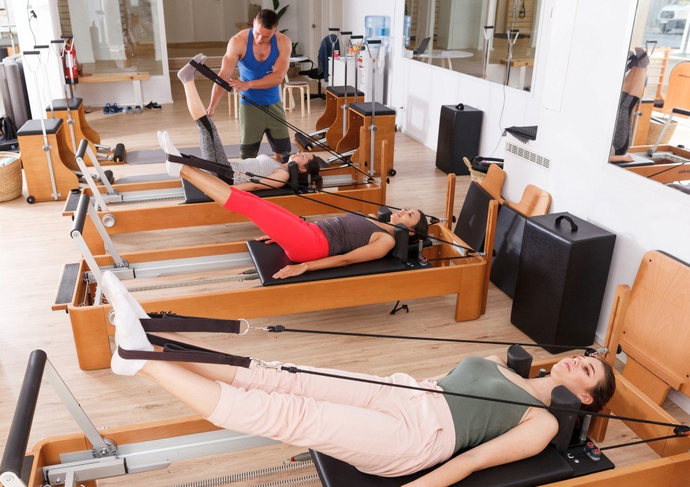 Safety on the Reformer Machine Group reformer classes with ladies doing leg in straps exercises and wearing Pilates grip socks.