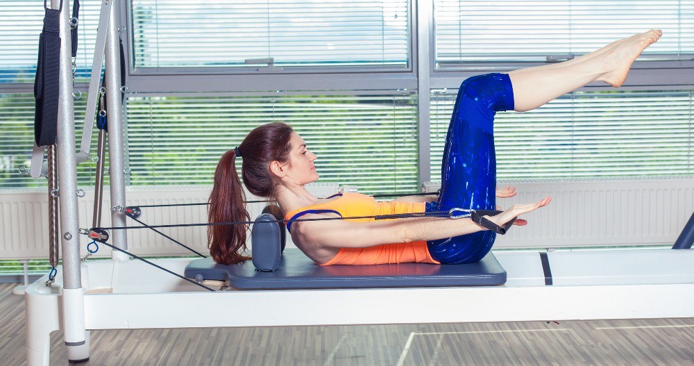 Set up of the Reformer machine Lady using the Allegro 2 reformer, in curl up position with hands reaching towards to front of the reformer working the abdominals.