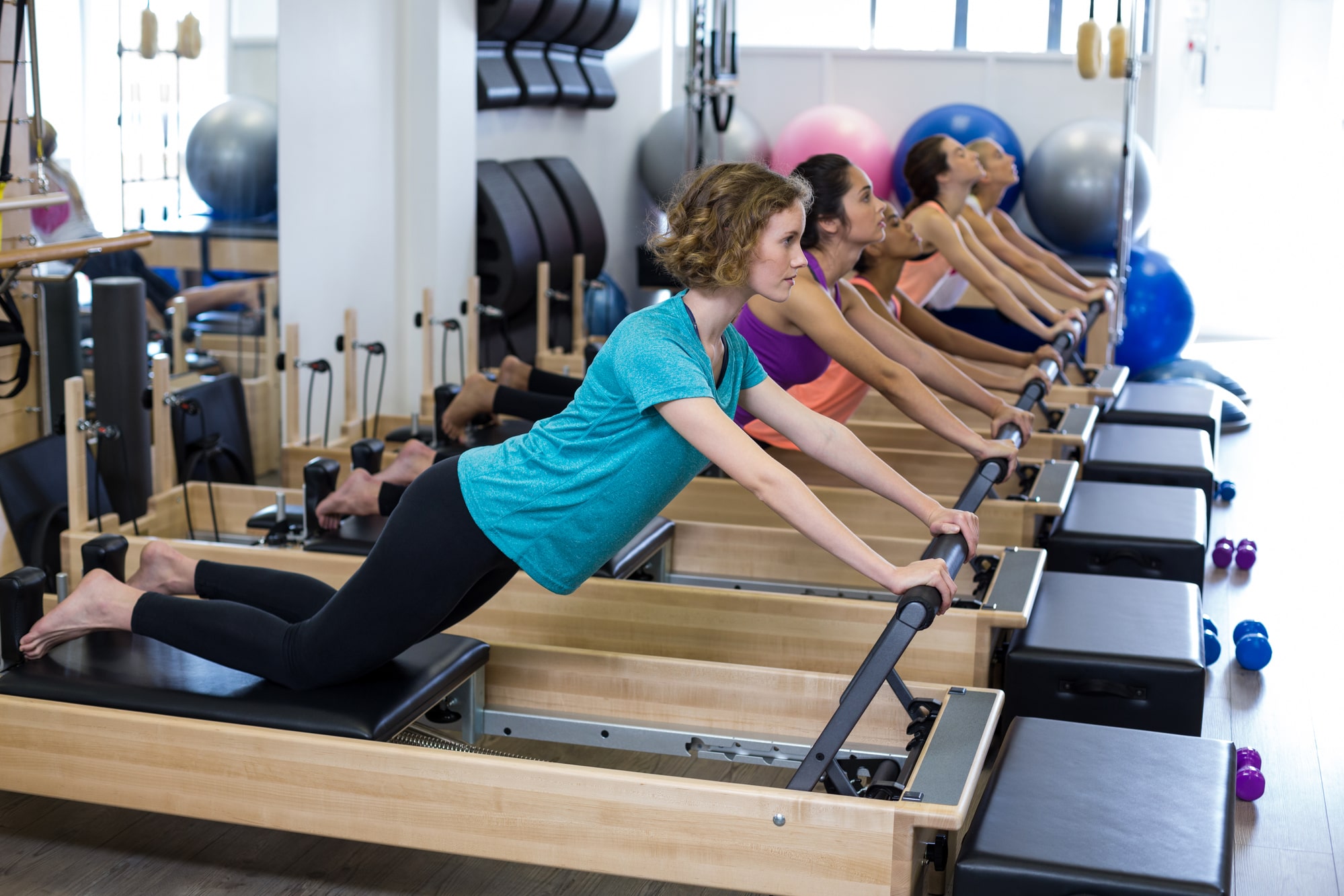 Group of Pilates students in studio doing half plank, on knees with hands on foot bar and feet back into shoulder blocks