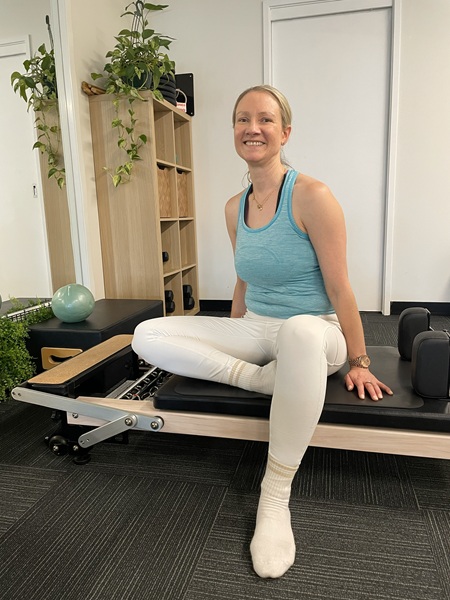 Victoria trained Pilates instructor sitting on side of Reformer